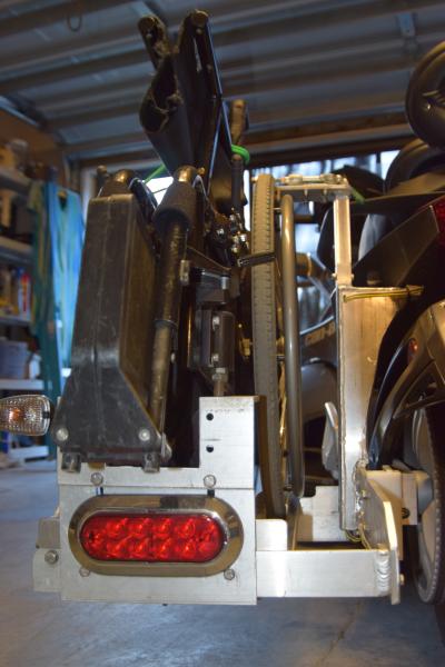 The rack is attached to the frame of the Spyder not the swing arm. It attaches just behind the passenger's left foot and just below the left turn sign